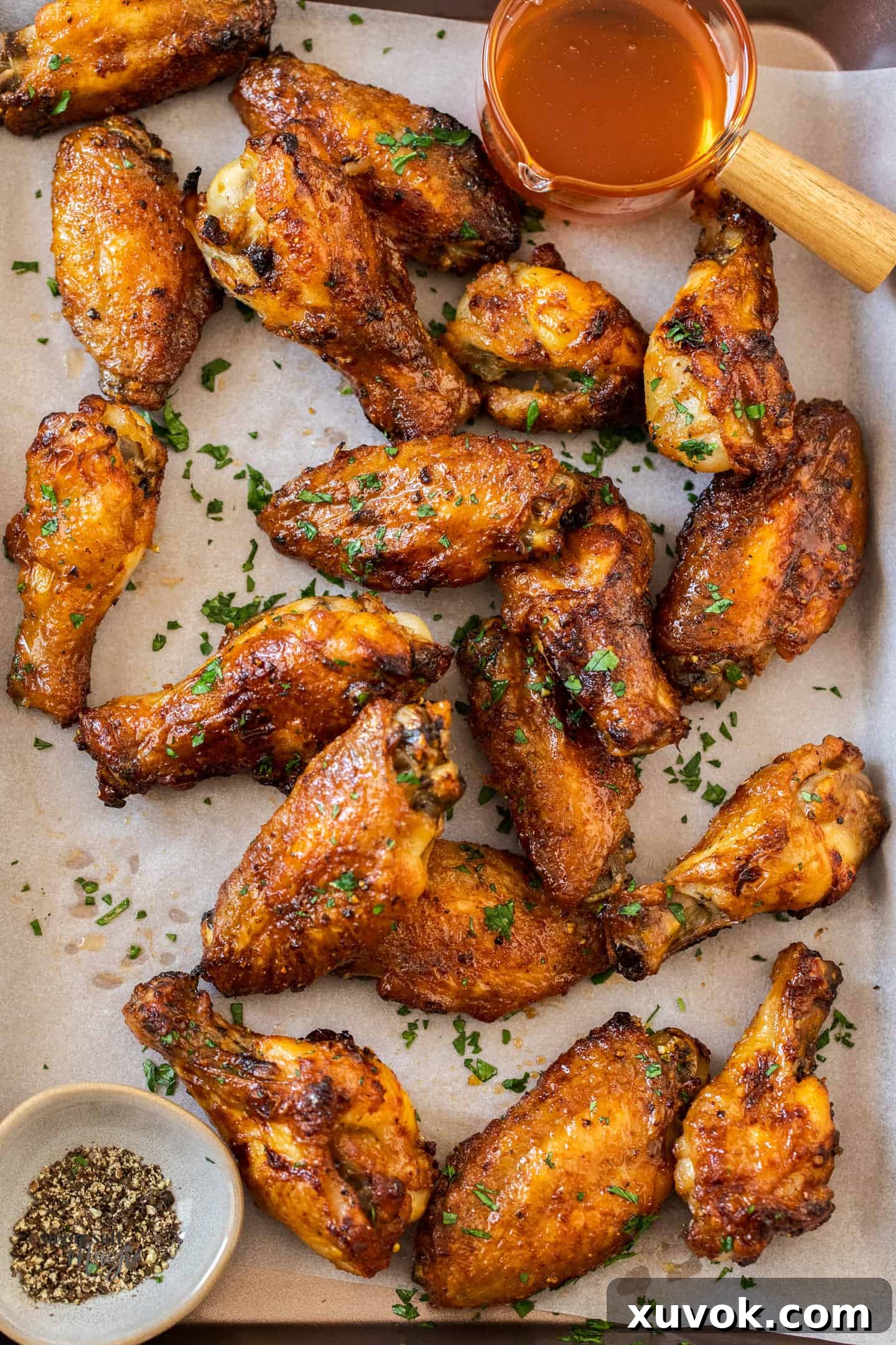 Golden baked chicken wings on a baking tray, ready to be coated with a pot of honey lemon pepper sauce.