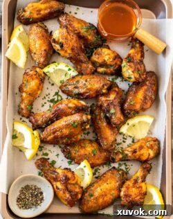 Top down view of golden chicken wings on a baking tray with lemon slices, ready to serve.