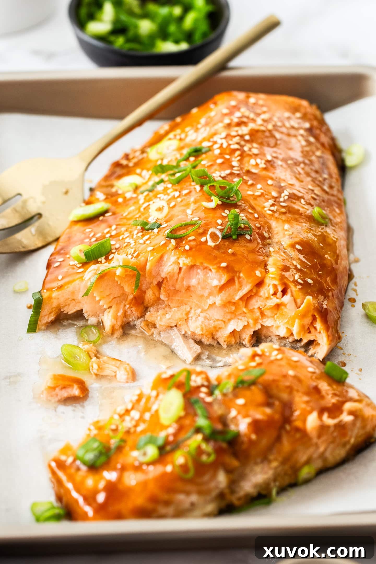 A large slab of oven-baked teriyaki glazed salmon, artfully broken open to reveal its moist, tender, and flaky interior.