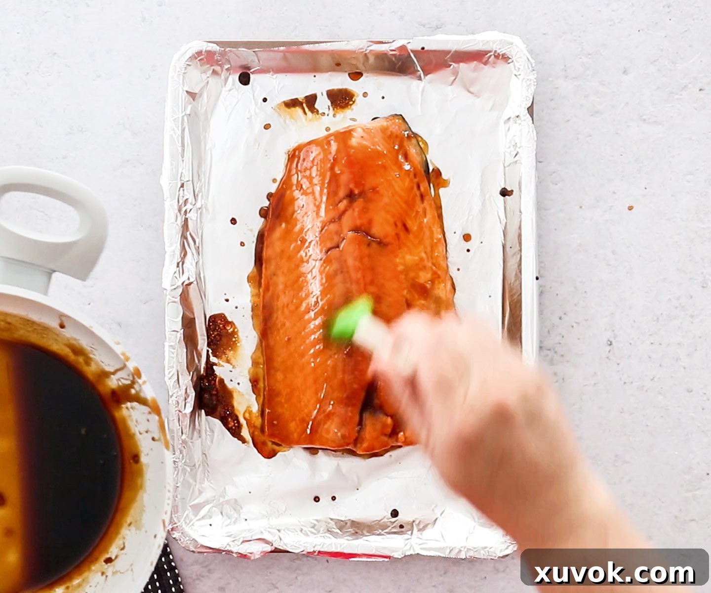 Raw salmon on a baking tray, being generously brushed with the shimmering teriyaki glaze, ready for the oven.