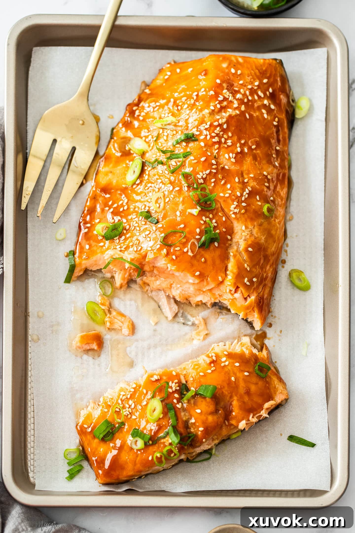 A vibrant top-down view of beautifully glazed teriyaki salmon, served on a baking tray, garnished with green onions and sesame seeds.