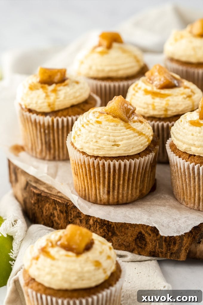 A cluster of beautifully frosted Apple Pie Cupcakes sitting on a rustic wooden cake board, ready to be enjoyed.
