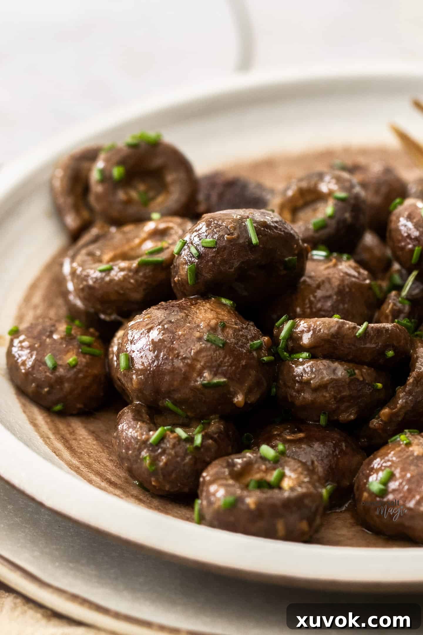 Roasted miso mushrooms piled onto a plate, scattered with fresh chives, highlighting their rich, glossy texture.