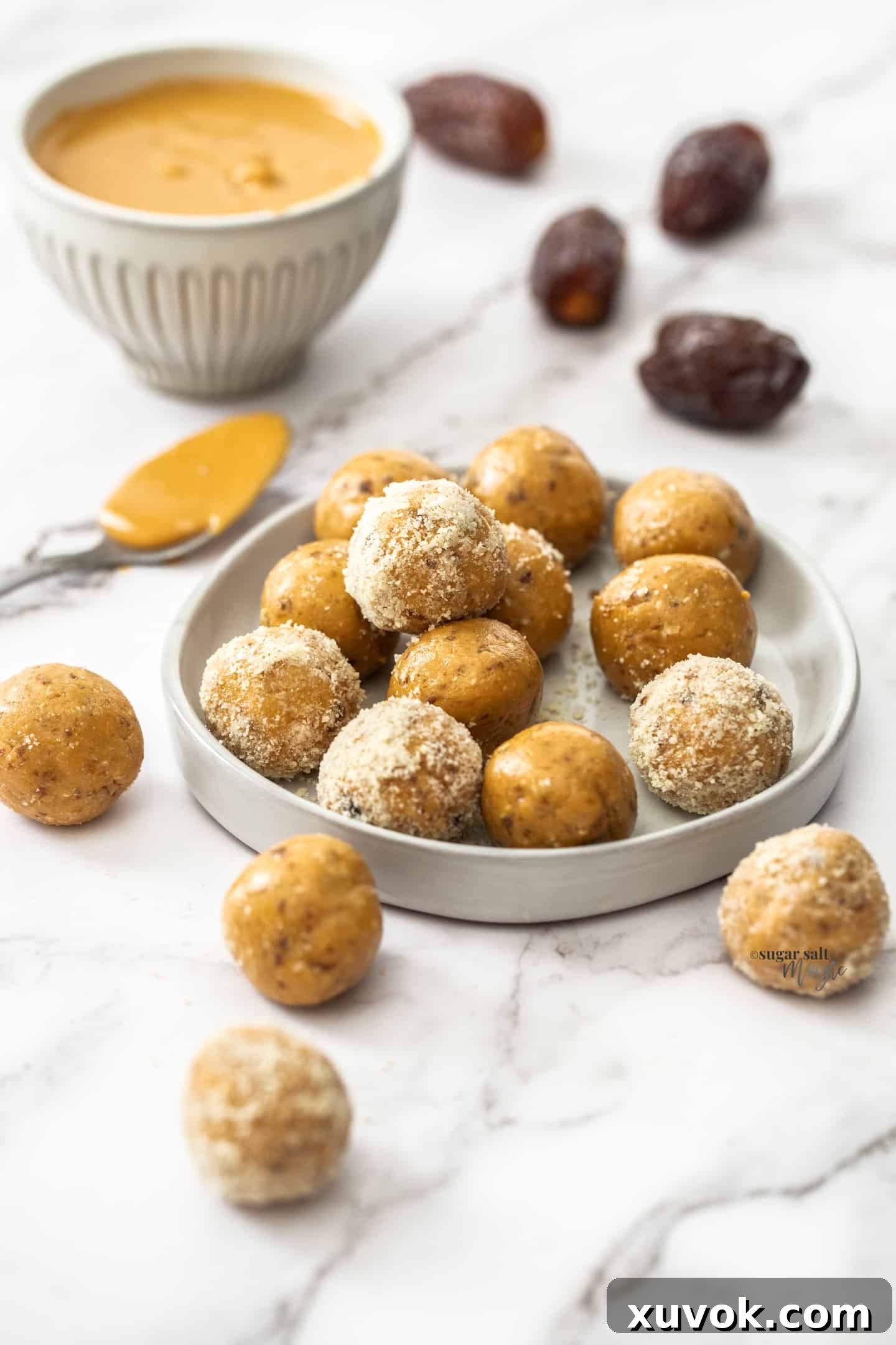 A batch of peanut butter bliss balls on a small dish with dates in the background. Freshly made, these no-bake energy bites are a healthy snack alternative.