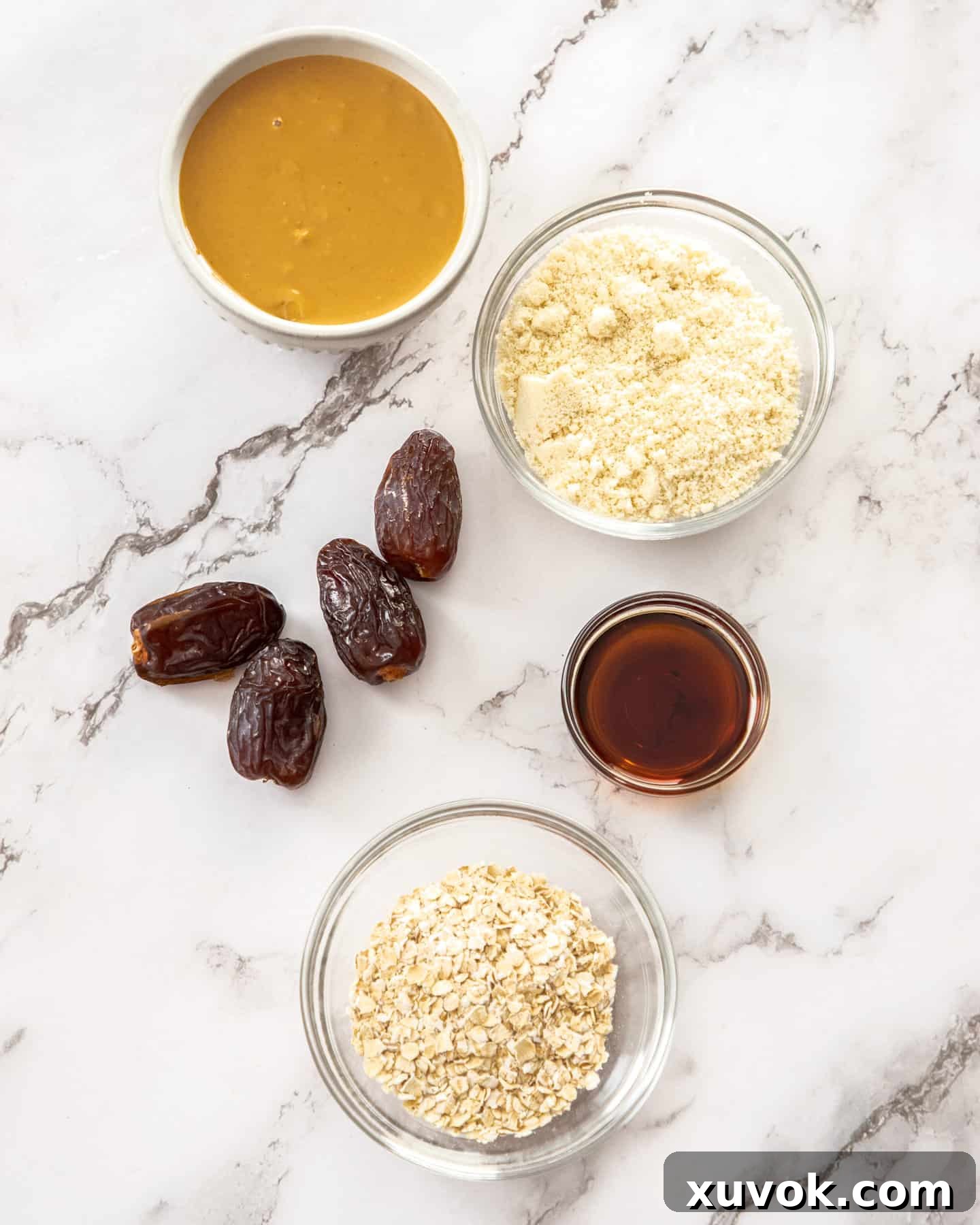 Ingredients for peanut butter bliss balls on a marble benchtop. Natural peanut butter, oats, almond flour, dates, and maple syrup are displayed.