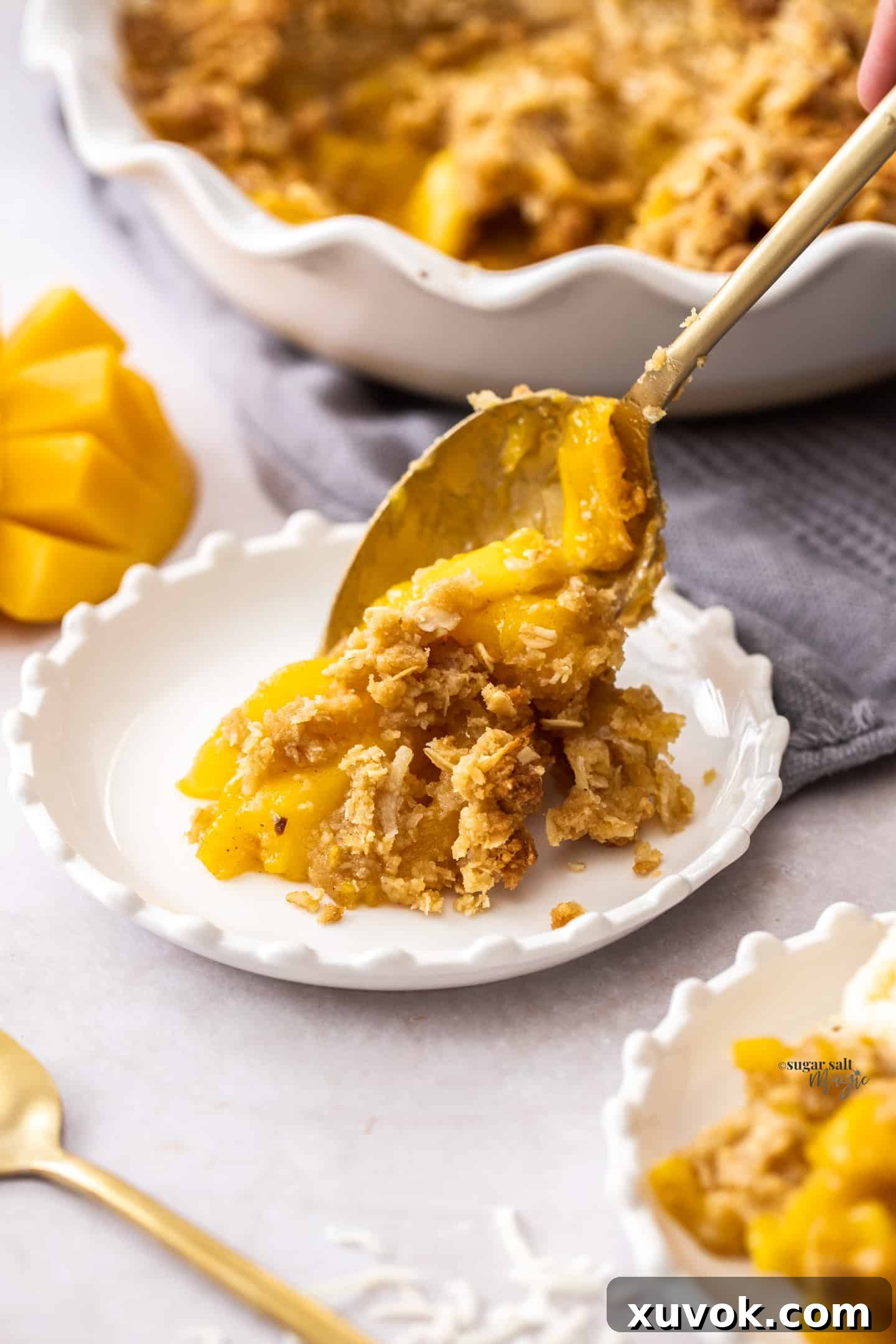 A golden spoon delicately scooping a generous portion of warm coconut mango crumble onto a small, elegant dessert plate, showcasing its golden, crunchy topping and soft, luscious mango filling.