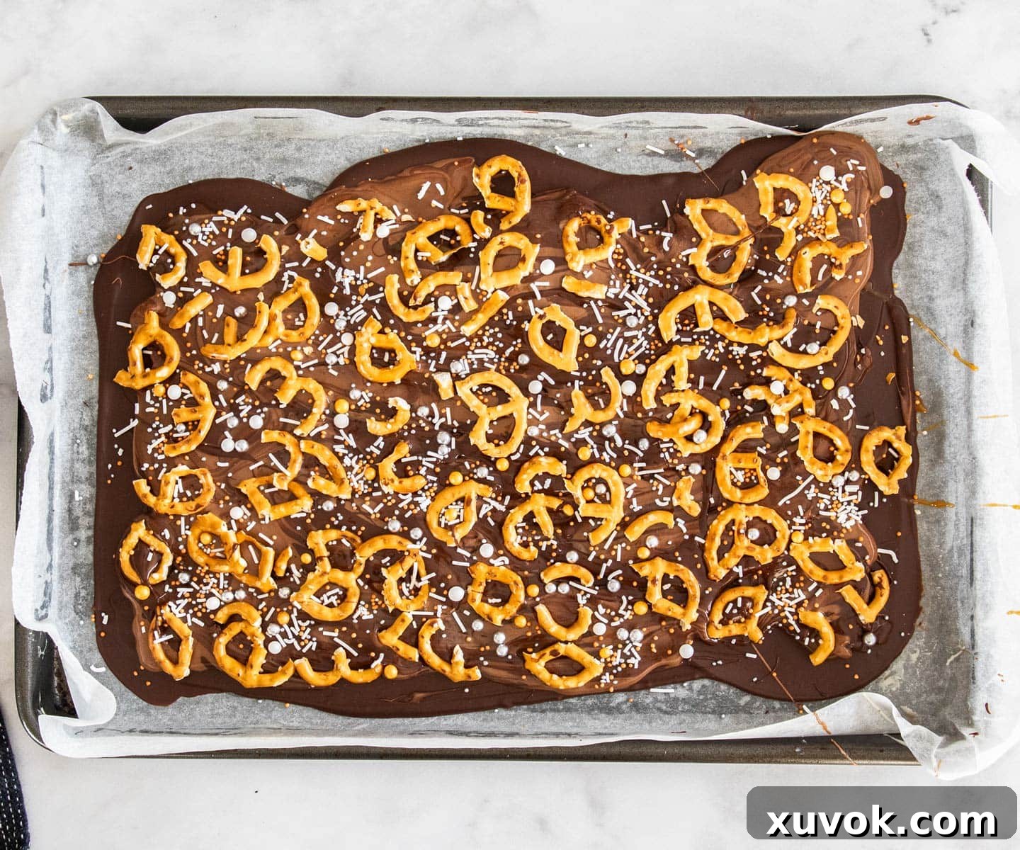 Top down view of the caramel pretzel bark adorned with pretzels and sprinkles, ready for chilling.