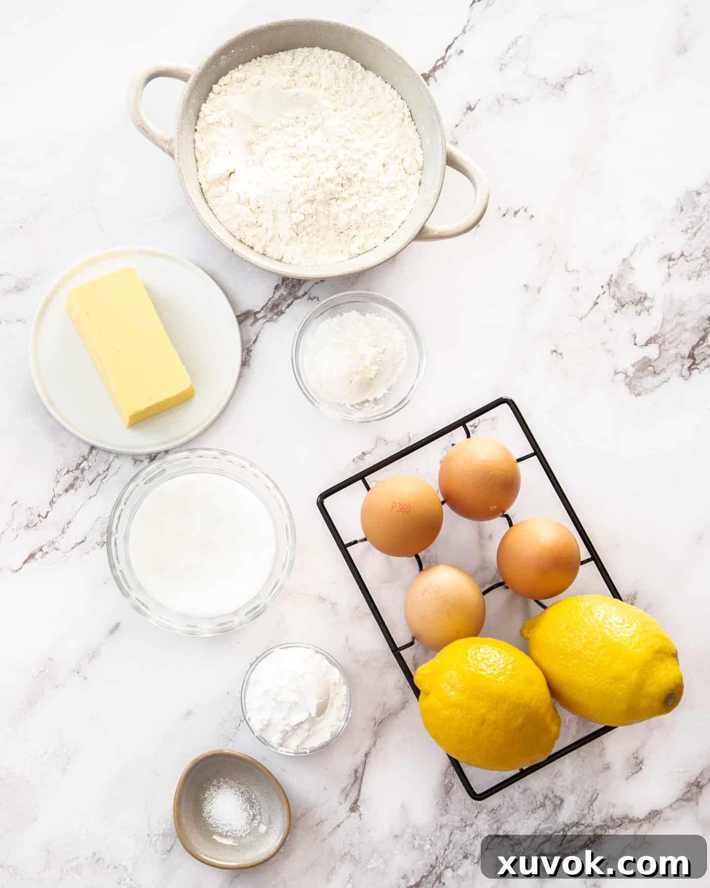 All the fresh ingredients for homemade lemon tartlets neatly arranged on a pristine marble surface.