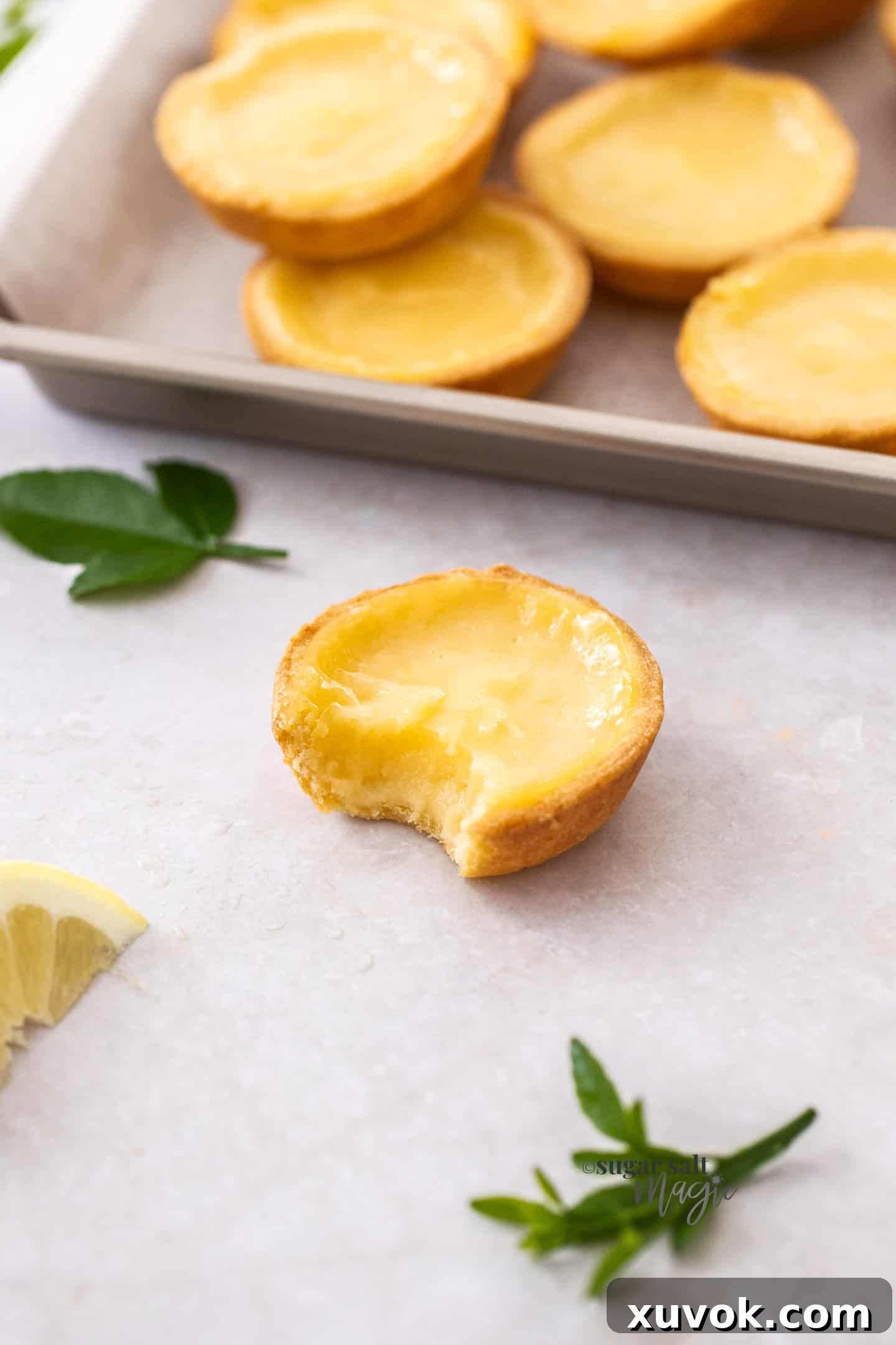 A close-up shot of a lemon tartlet with a bite taken, revealing the vibrant lemon curd and flaky pastry.
