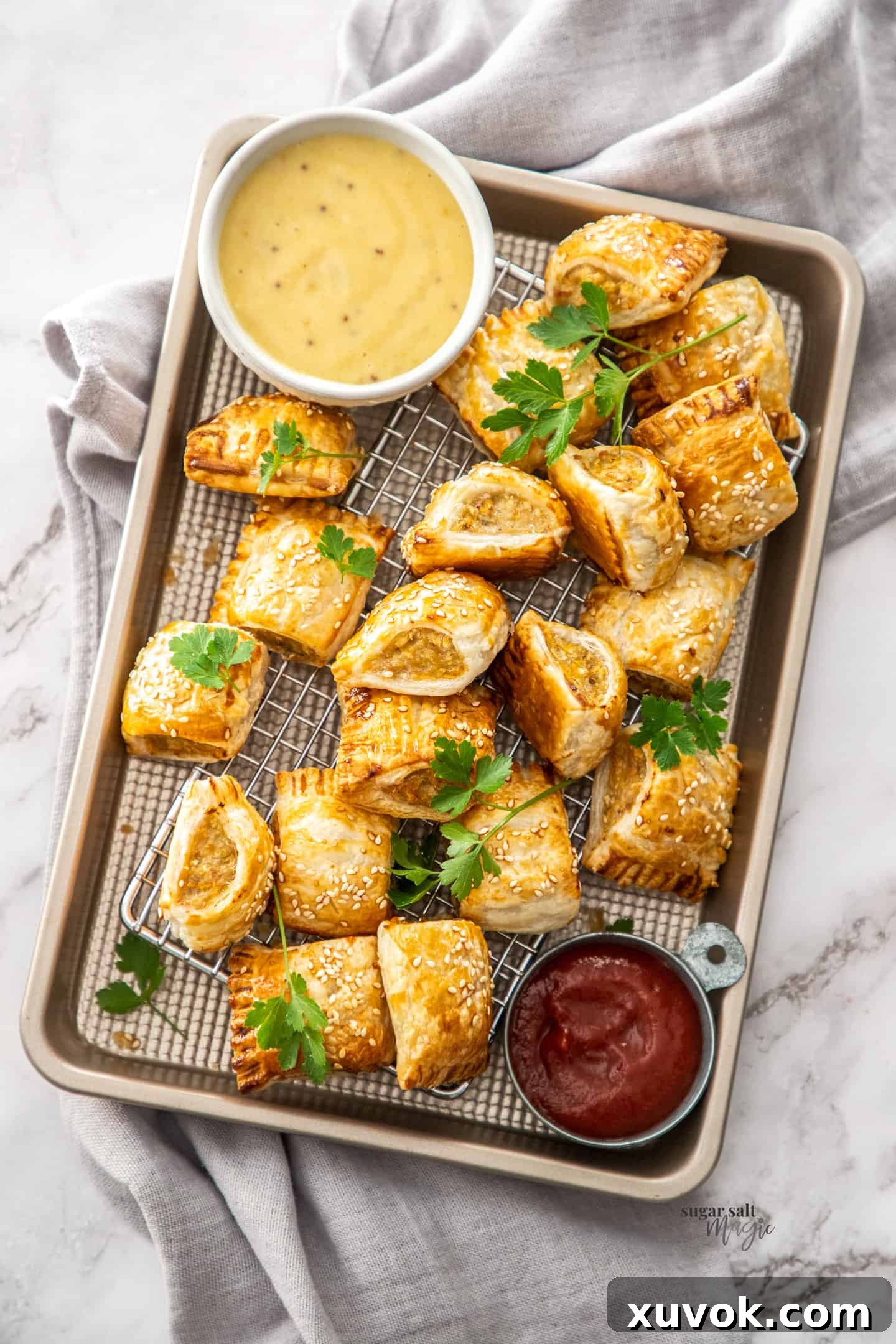 Top down view of a pile of golden-brown chicken sausage rolls on a wire rack in a baking tray, ready to be served.