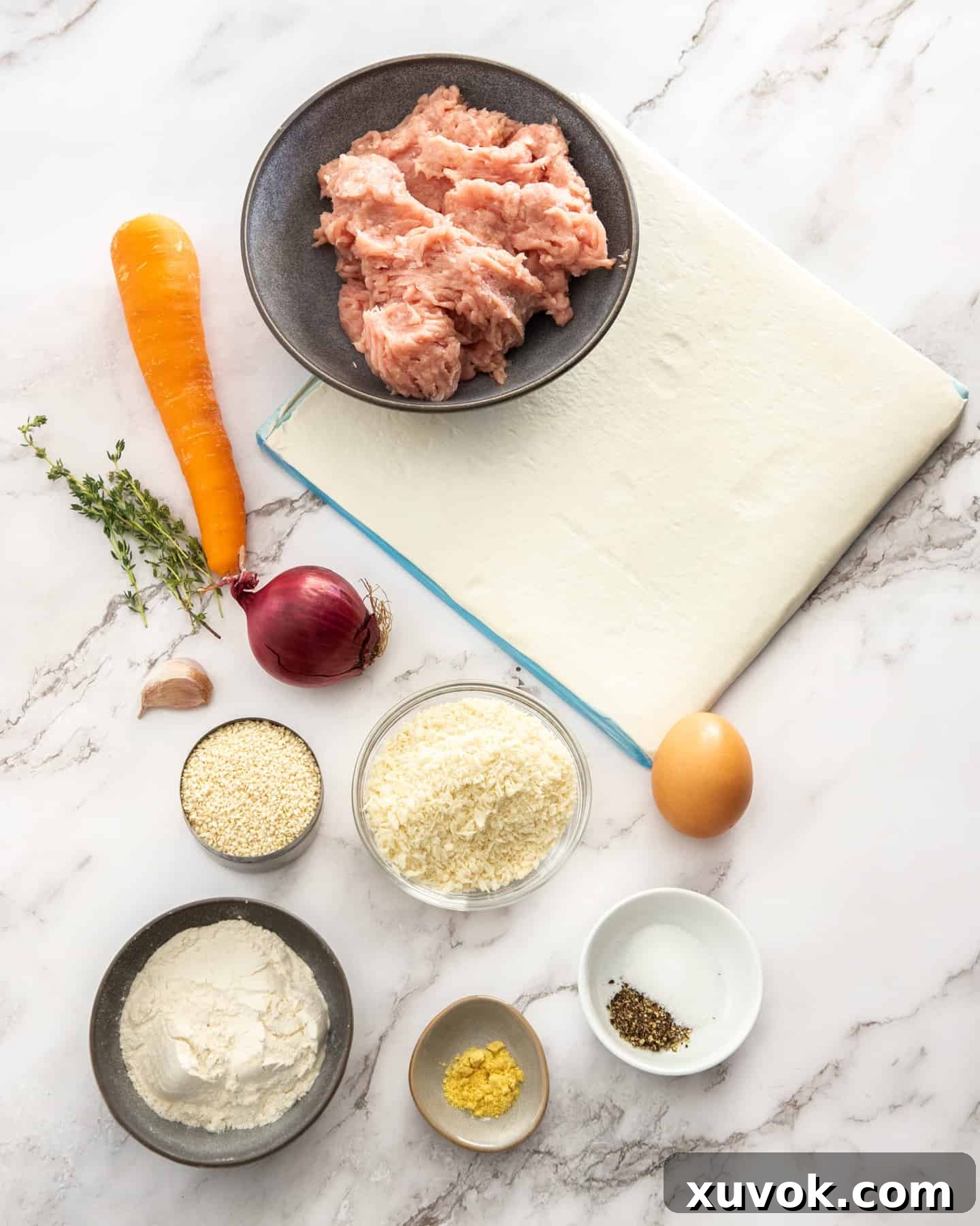Assorted ingredients for chicken sausage rolls, including chicken mince, grated vegetables, and herbs, arranged on a marble background.