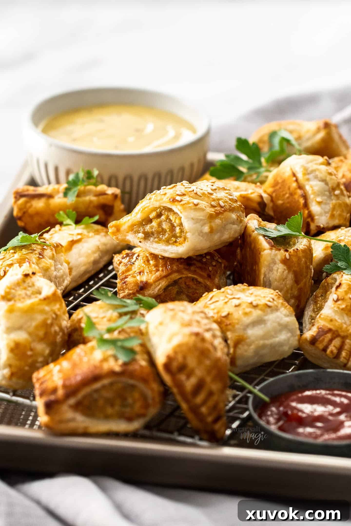 Crispy chicken sausage rolls piled high in a baking tray, with a small bowl of dipping sauce in the background.