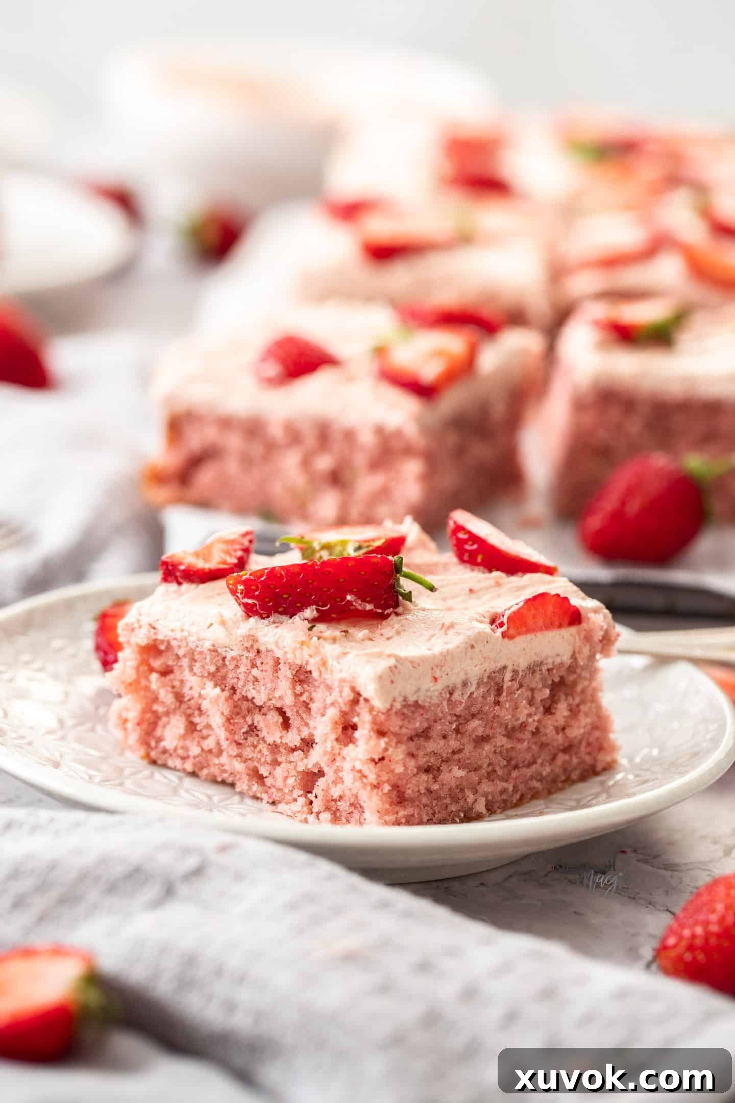A square slice of strawberry cake on a small white dessert plate, showing the layers.