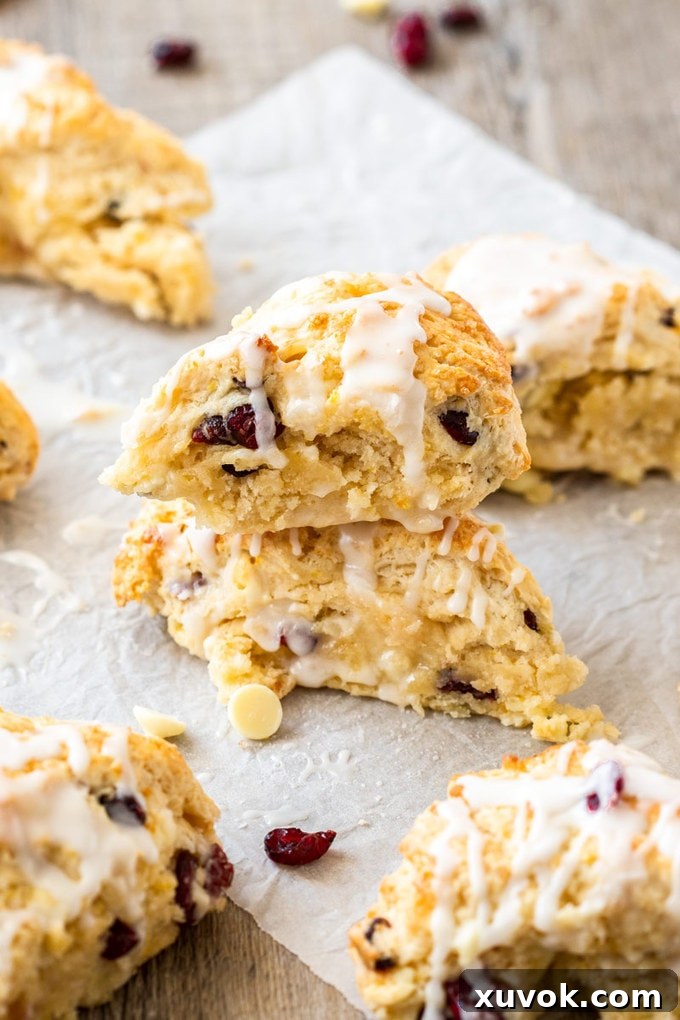 A stack of two beautifully baked cranberry scones, surrounded by more golden brown scones on a baking sheet.