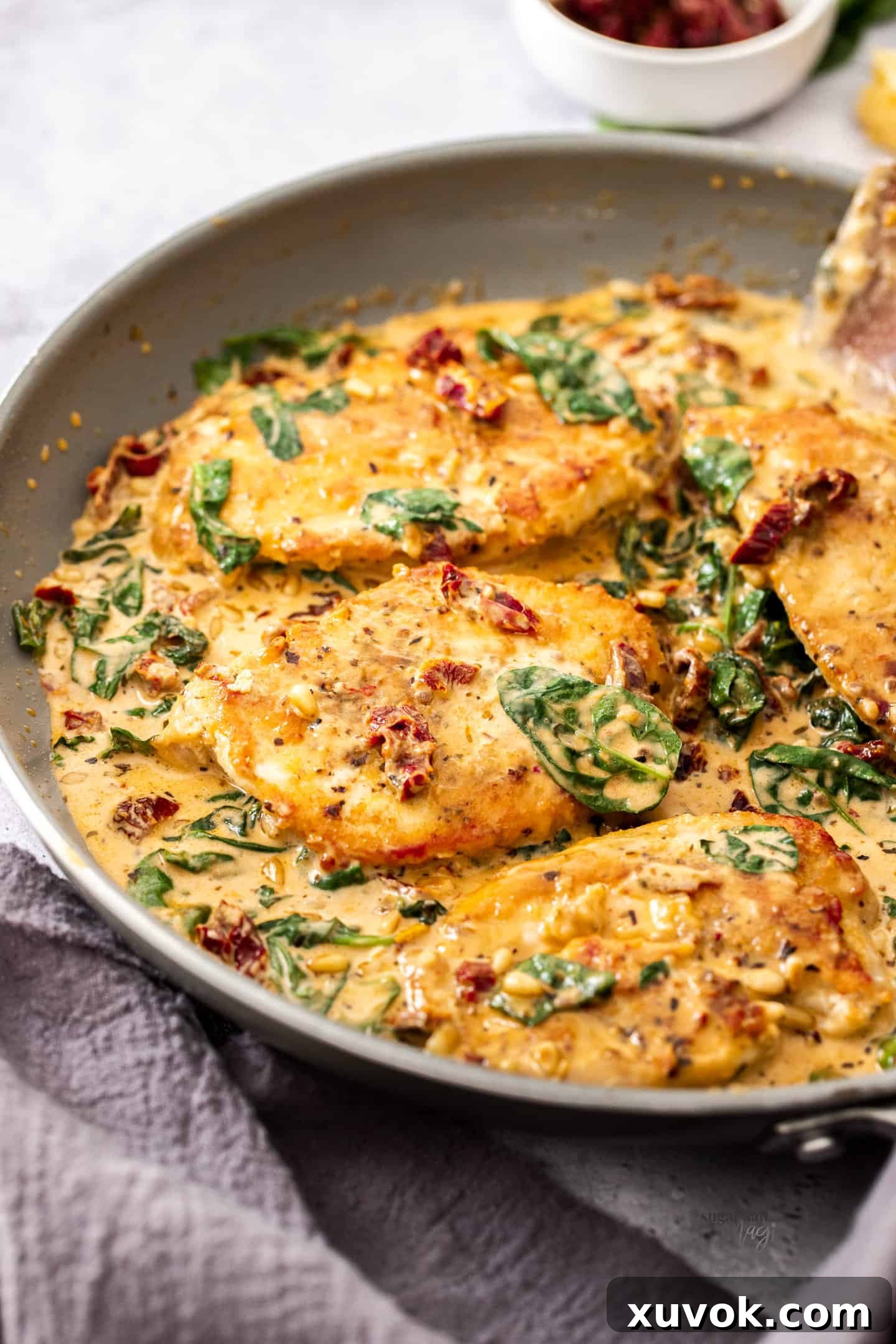 3 pieces of cooked chicken in a skillet with a creamy sauce, garnished with fresh basil.