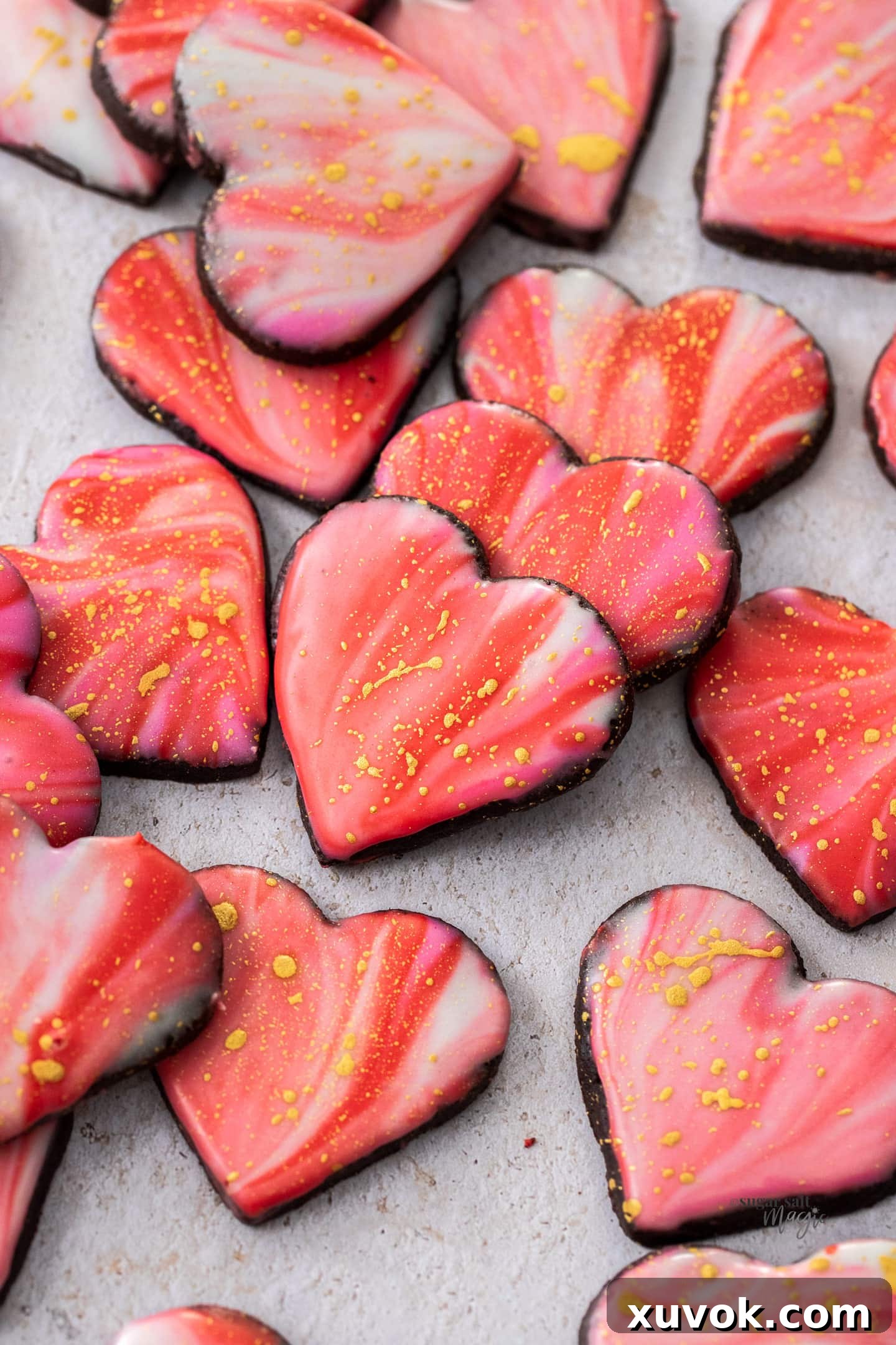 A pile of heart shaped iced sugar cookies on a stone surface.