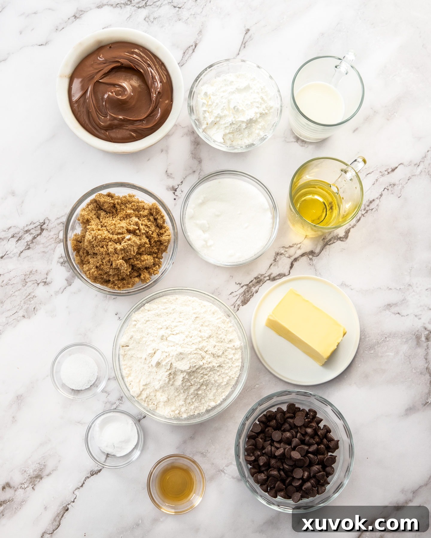 A vibrant collection of ingredients for chocolate chip Nutella bars, neatly arranged on a pristine marble surface, ready for baking.