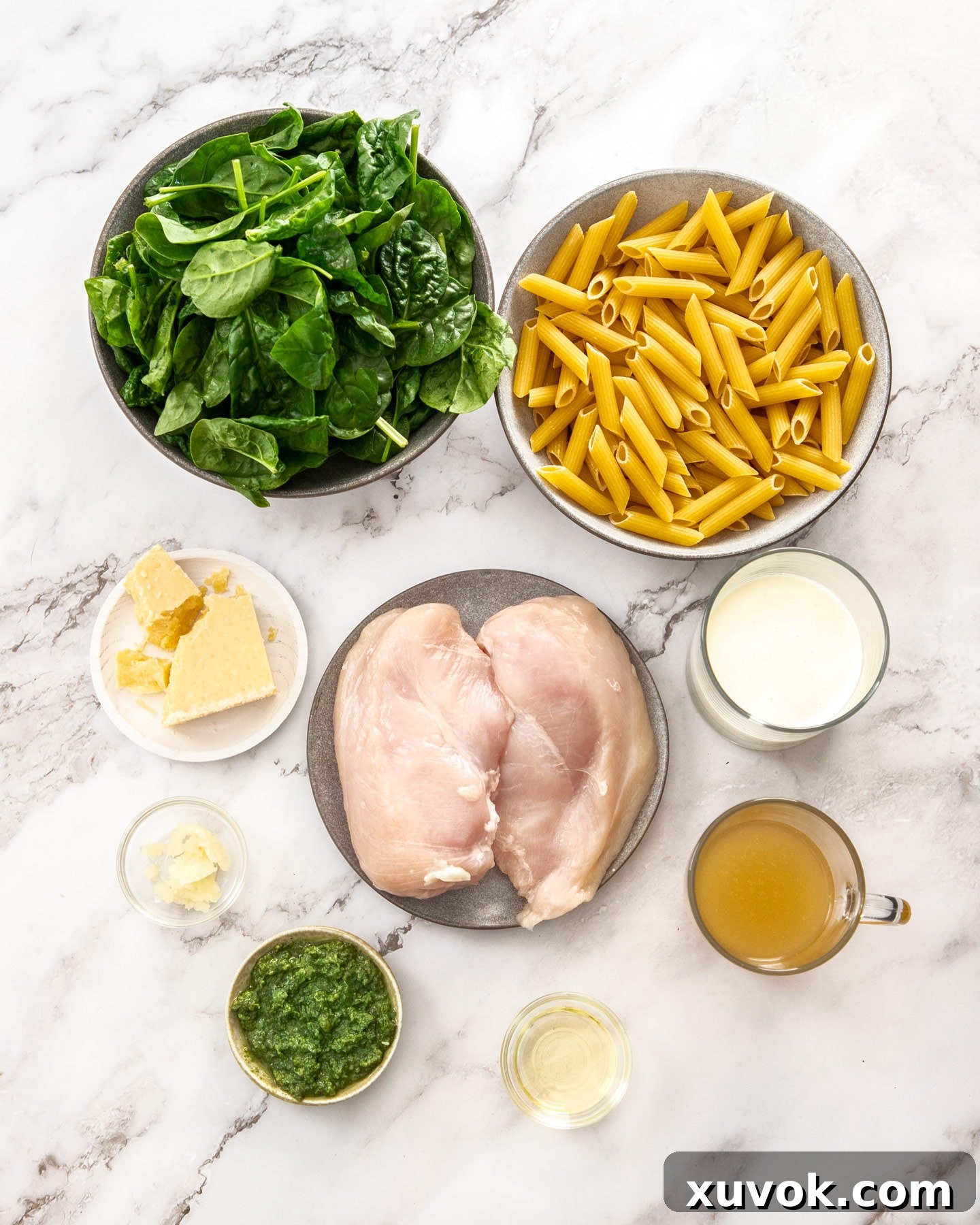 Ingredients for creamy chicken spinach pasta laid out on a marble surface.