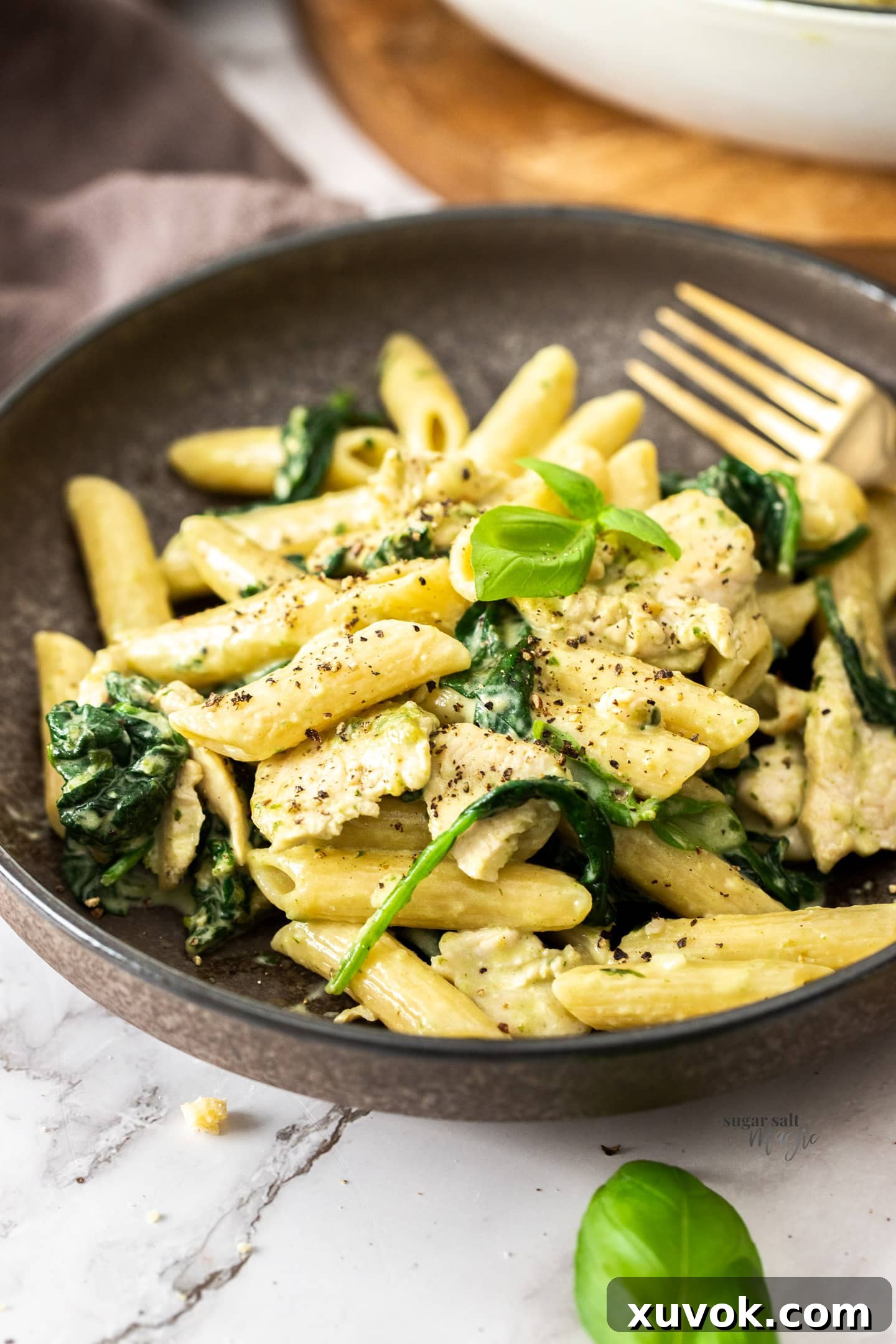 A brown bowl filled with creamy pasta chicken and spinach, garnished with fresh herbs.