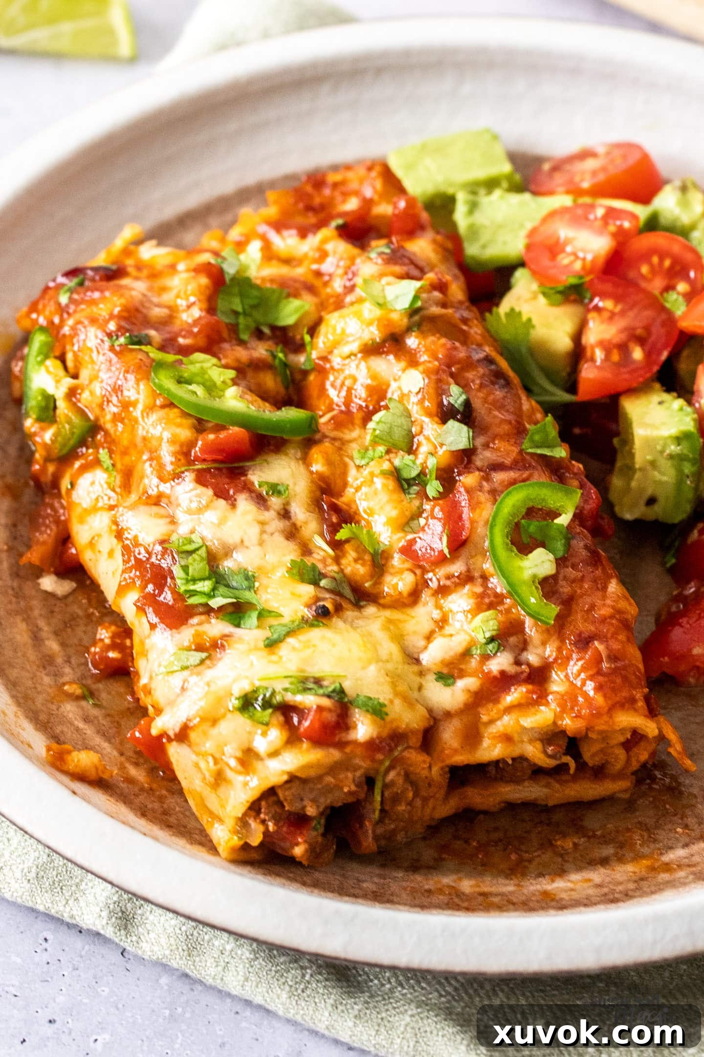 Enchiladas on a plate next to an avocado and tomato salad.