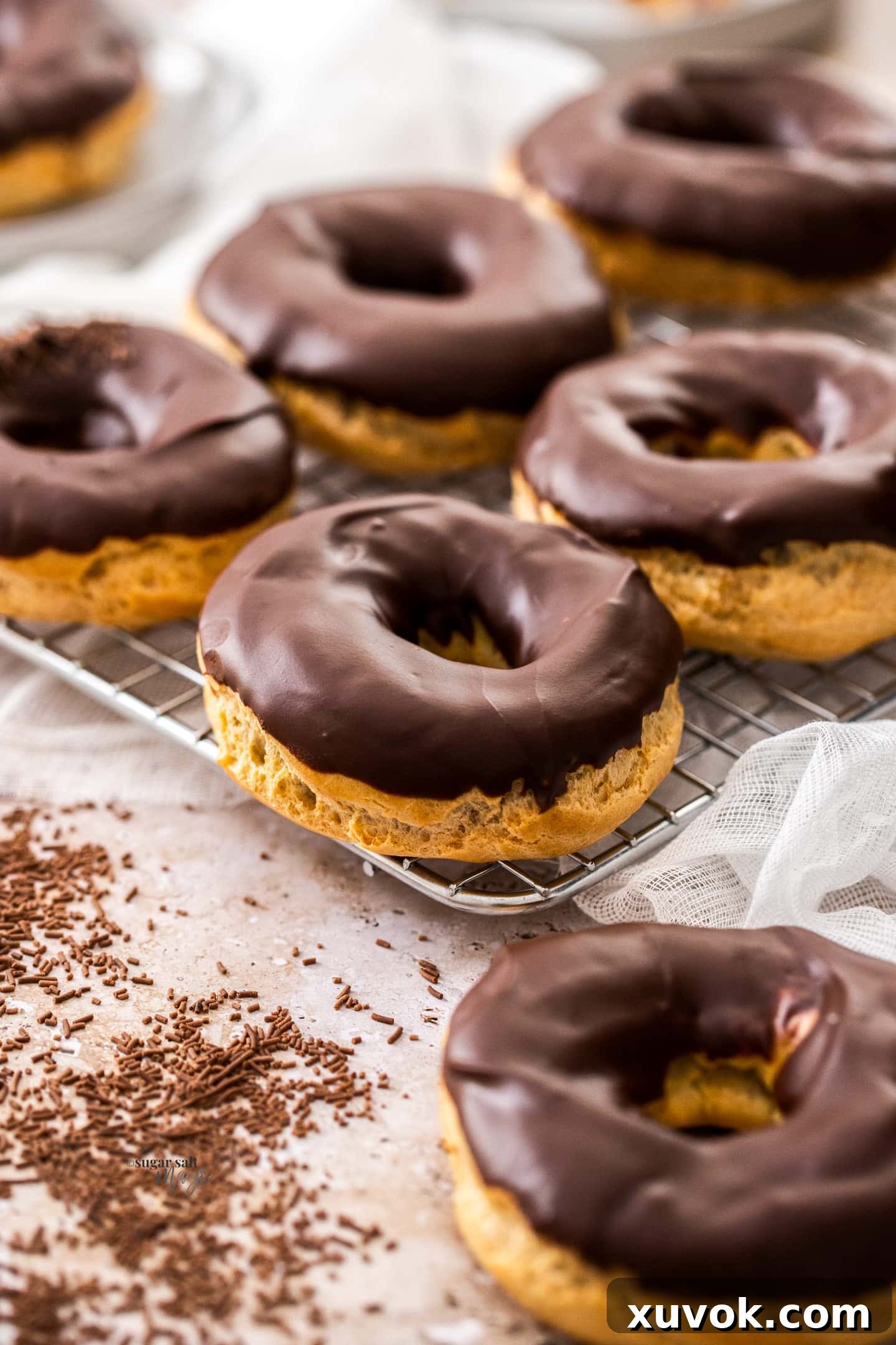 A freshly baked batch of chocolate chouxnuts cooling on a wire rack, glistening with chocolate glaze.
