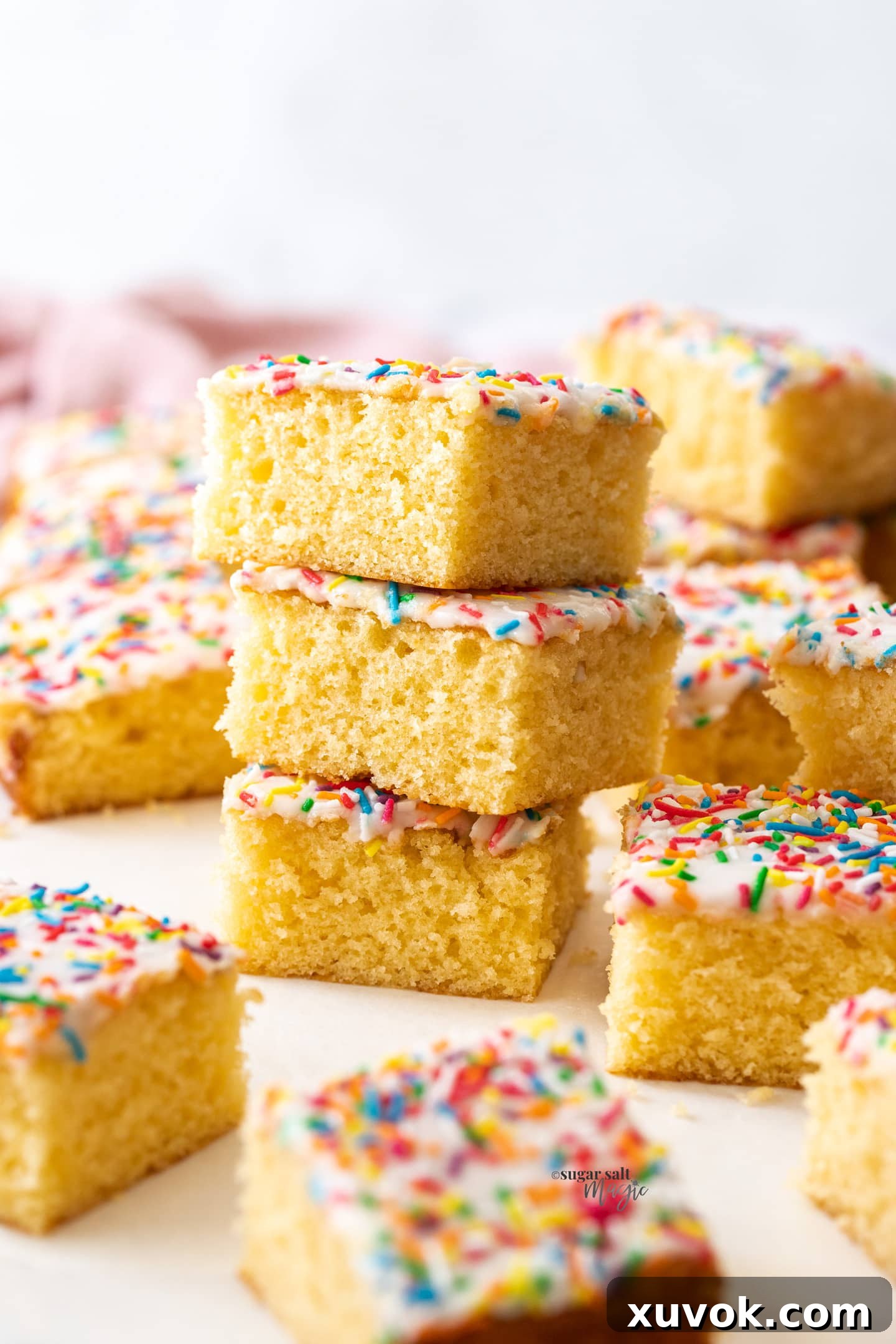 A perfectly arranged stack of three squares of vanilla sponge tray bake cake, showcasing its soft texture and inviting simplicity.