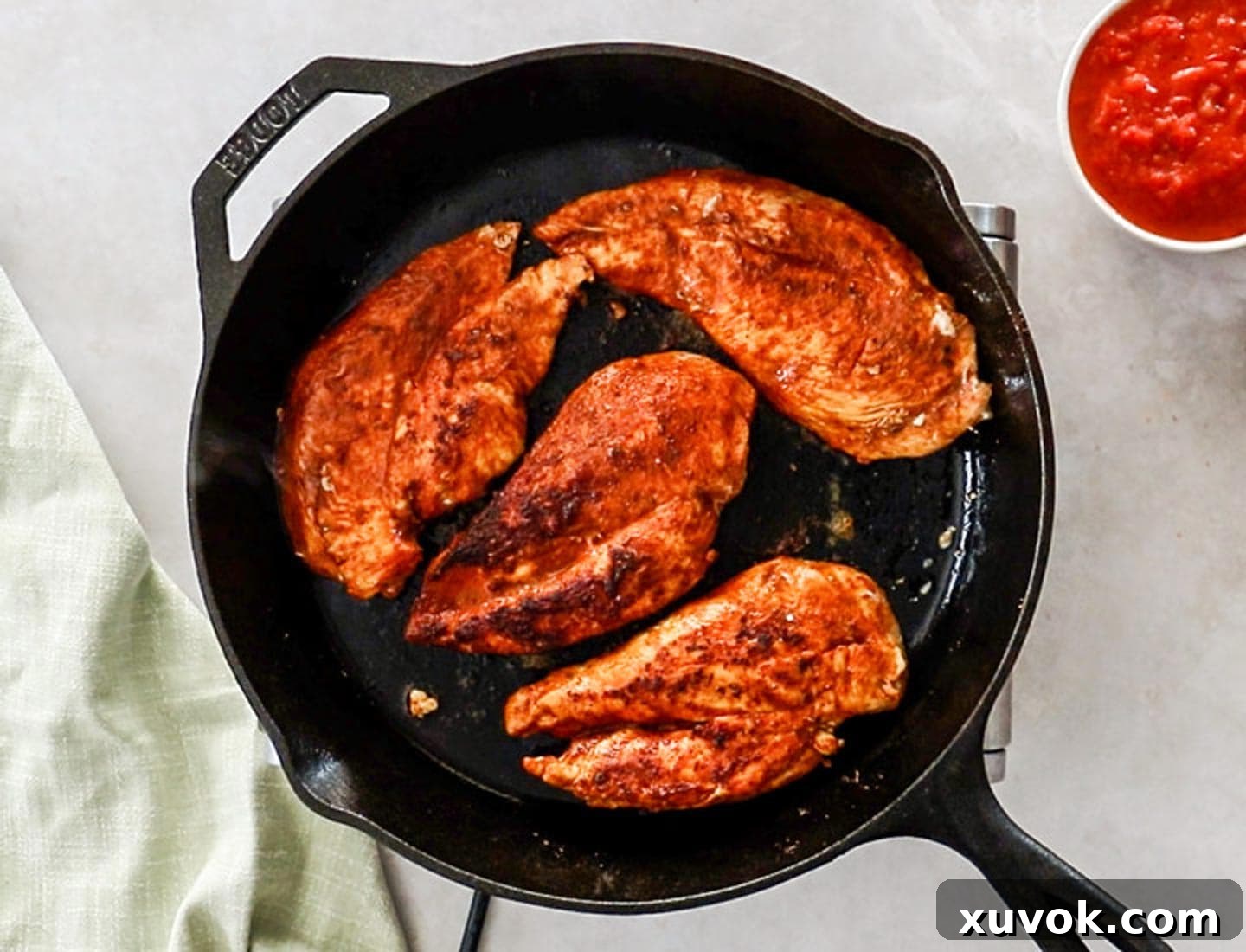 Four perfectly seasoned and seared chicken breasts, golden-brown and sizzling, nestled in a cast iron skillet on the stovetop.