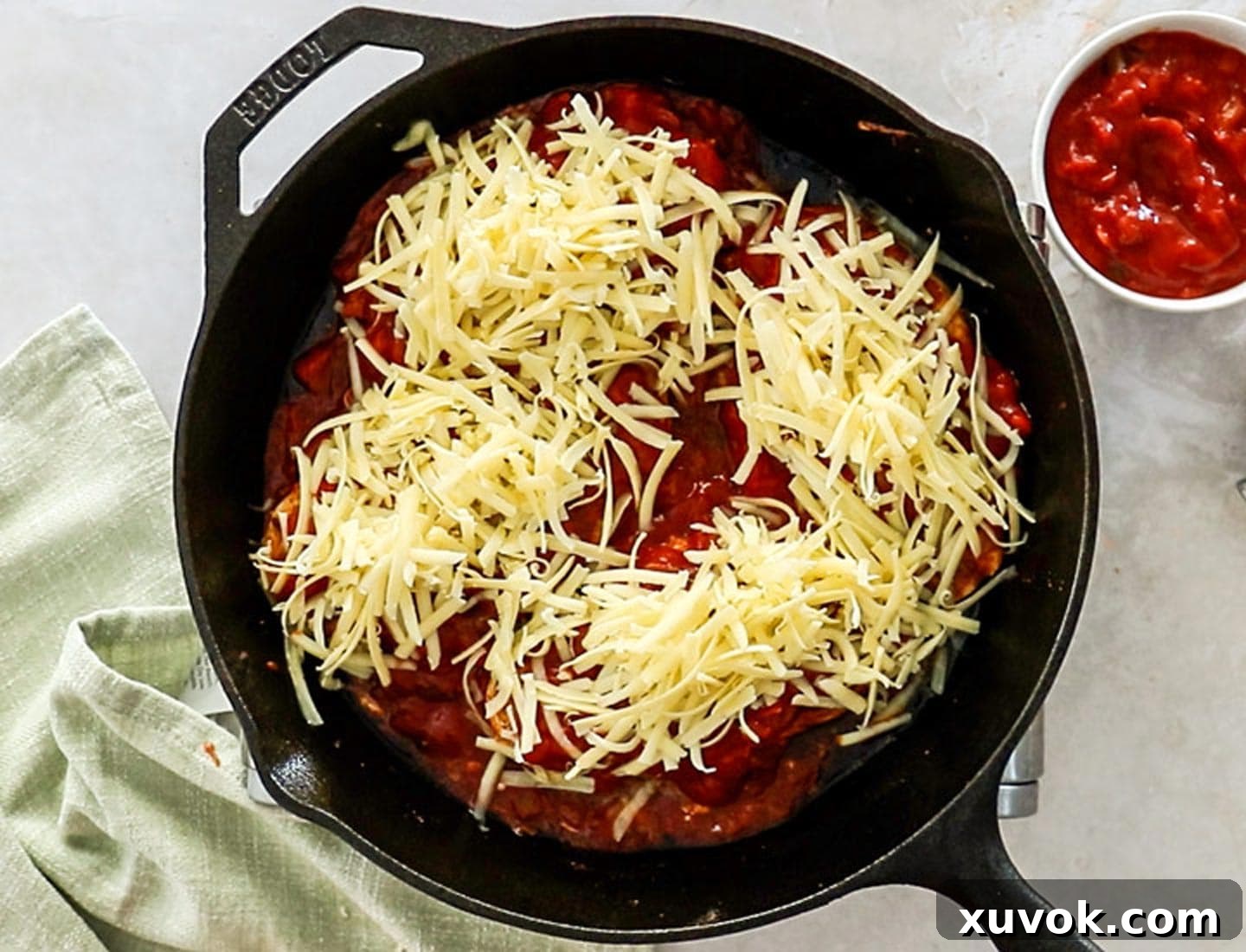 Seared chicken breasts generously topped with chunky tomato salsa and a blanket of shredded cheese, ready for baking in a cast iron skillet.