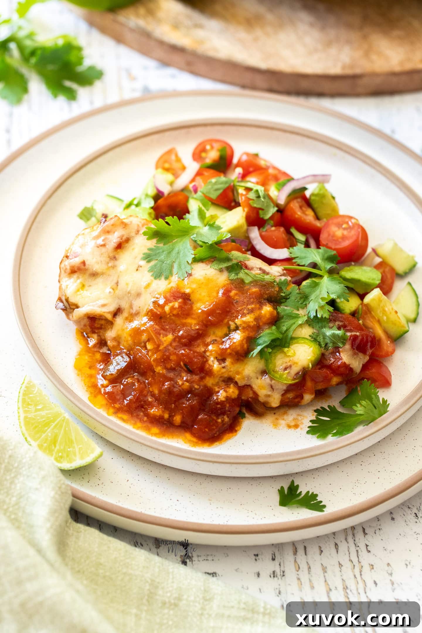 A glistening piece of cheesy salsa chicken breast on a plate, perfectly cooked and ready to eat, accompanied by a fresh side salad.