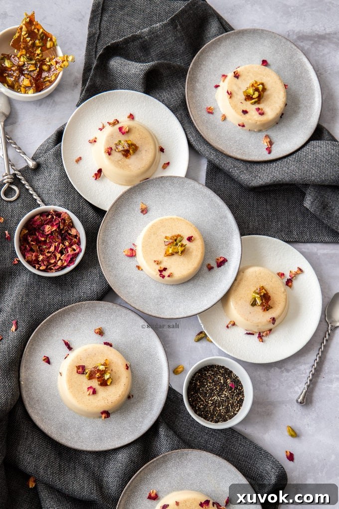 Six dessert plates on a table, each holding a beautifully presented Chai Panna Cotta with Pistachio Toffee, viewed from above.