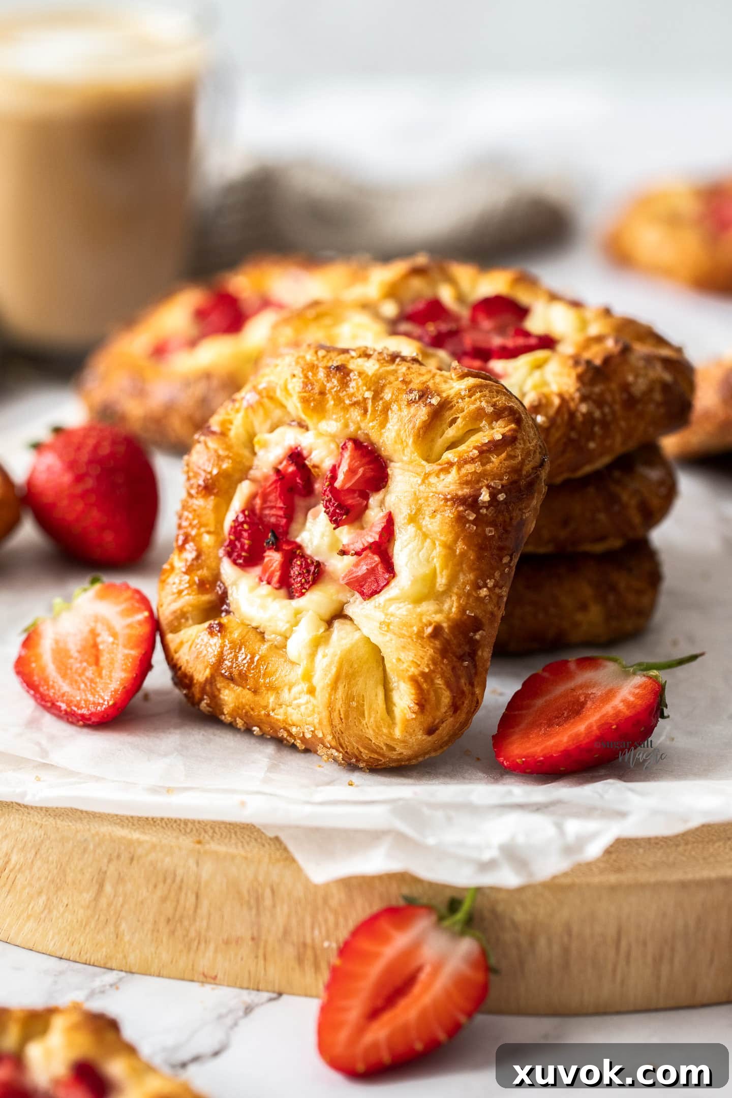 A stack of 3 strawberry Danishes with one leaning up against them, showcasing their golden-brown, flaky exterior and vibrant strawberry filling.