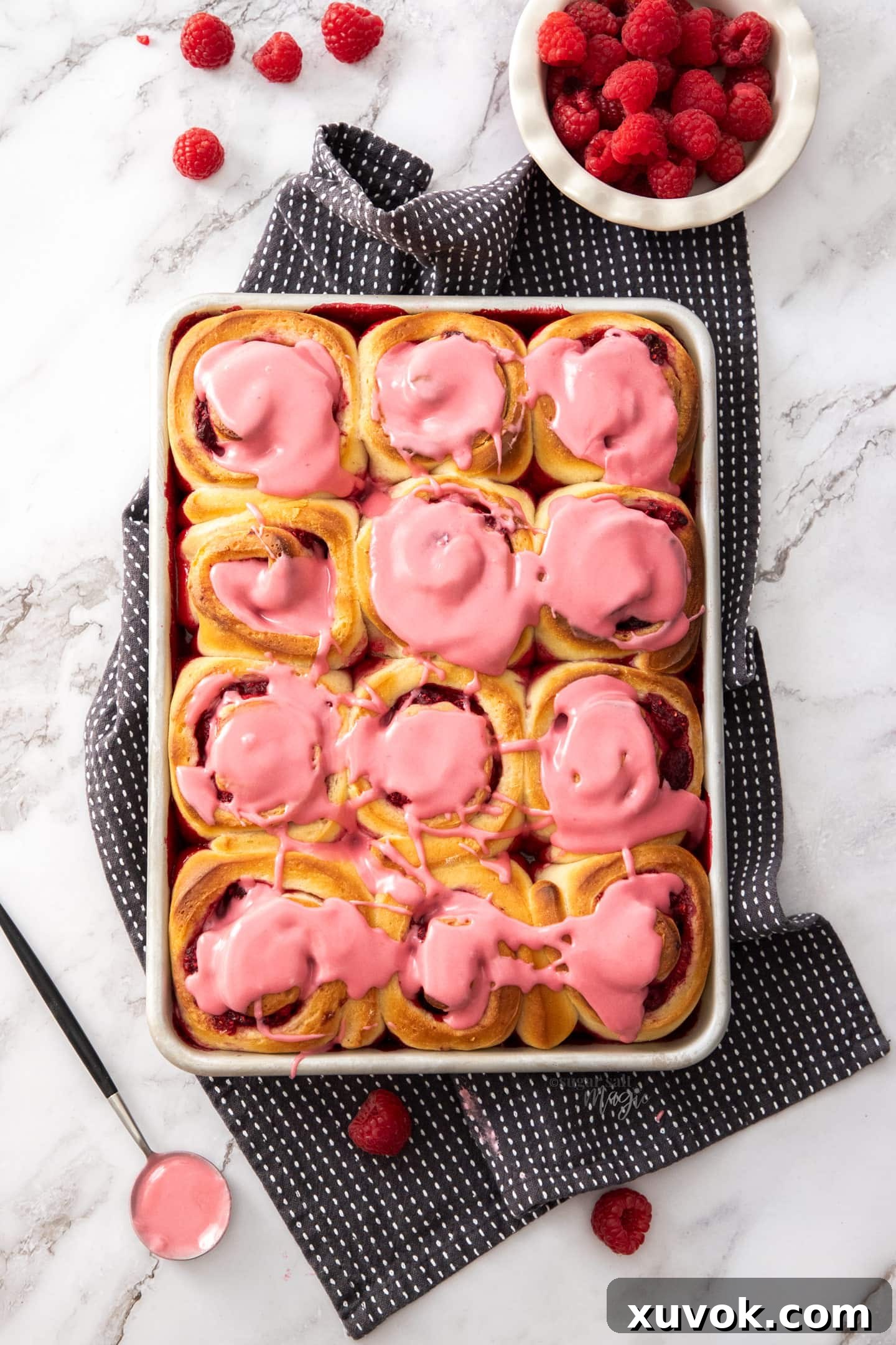 Top down view of a baking tray with 12 raspberry rolls.