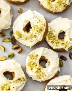 Closeup of 2 carrot cake donuts surrounded by pistachios.