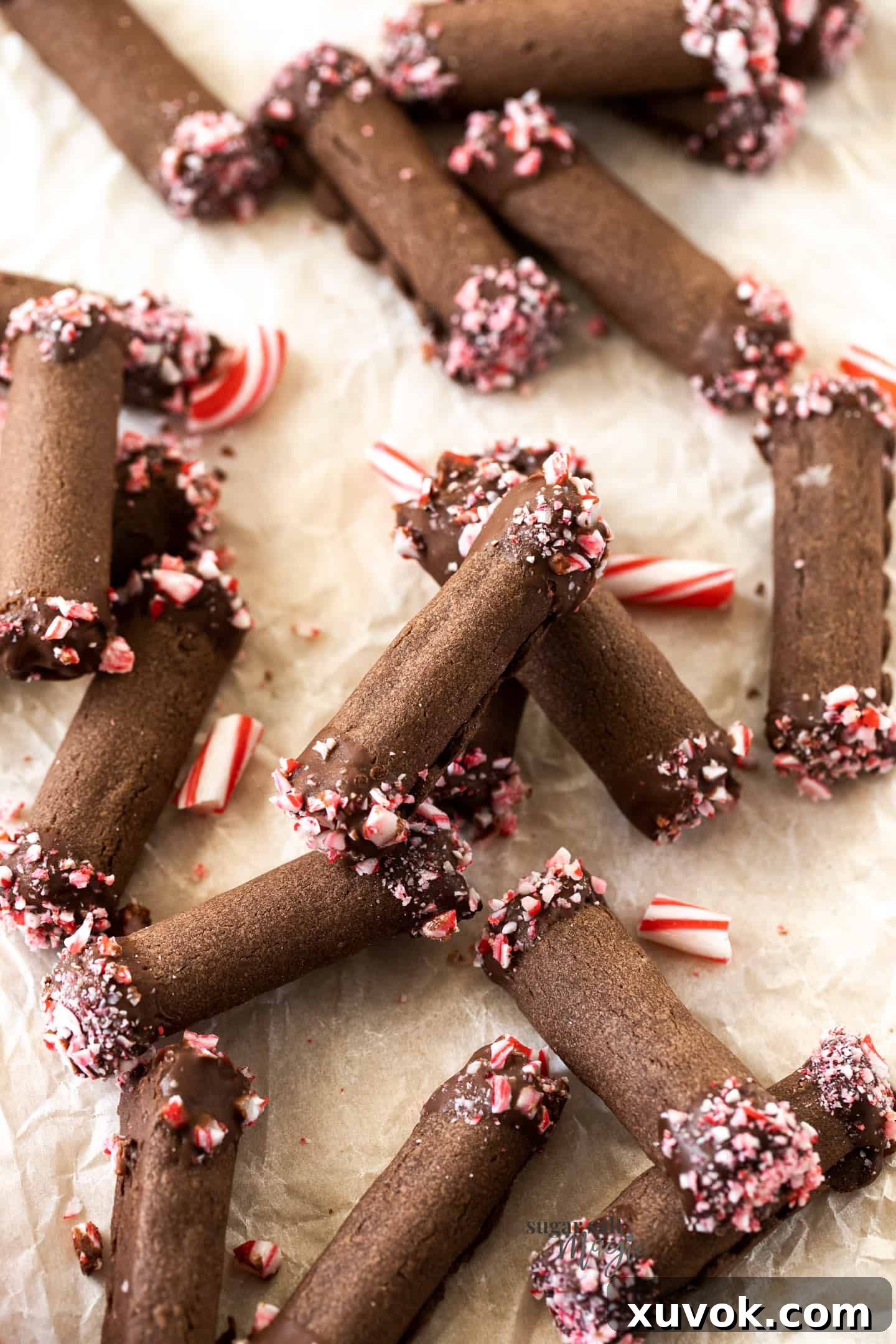 A batch of chocolate roll cookies on a sheet of baking paper, showcasing their perfect tubular shape and festive candy cane topping.