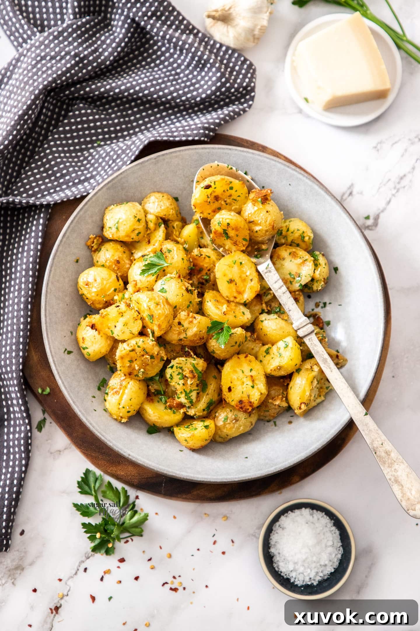 Top down view of a grey bowl filled with roasted potatoes. Golden brown and crispy, sprinkled with fresh herbs.