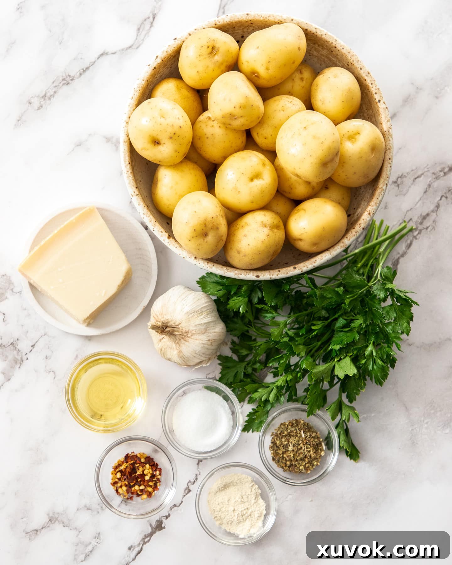 Ingredients for roasted parmesan garlic potatoes on a marble surface. Including potatoes, Parmesan cheese, garlic, and herbs.