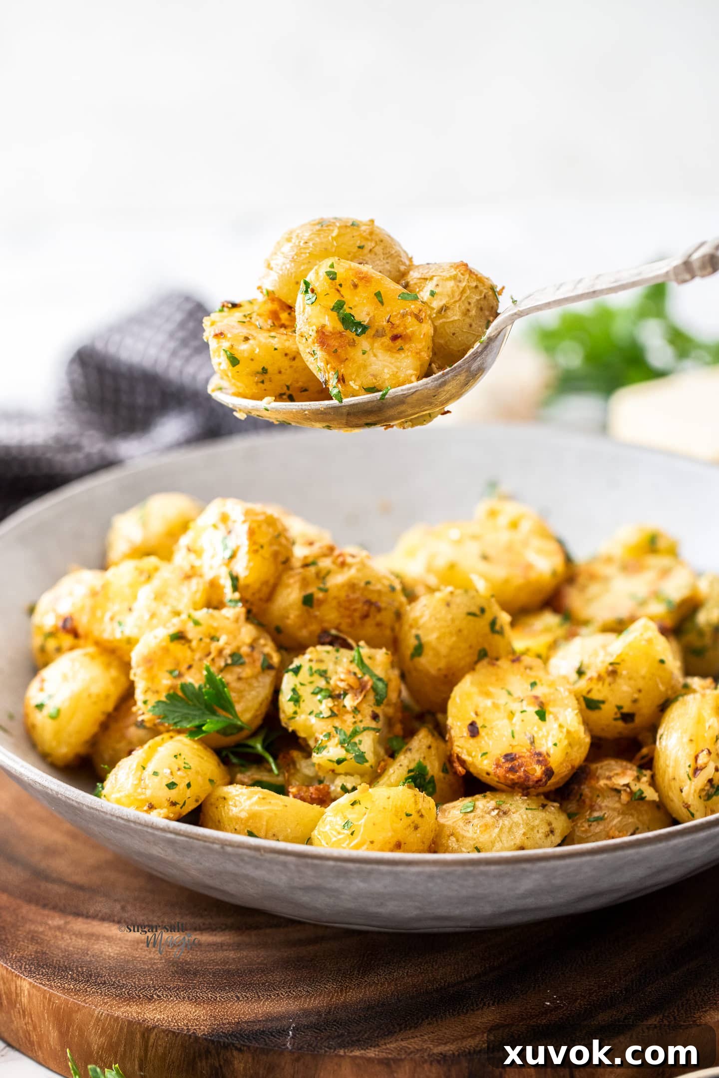 A spoon lifting roasted potatoes out of a grey bowl.