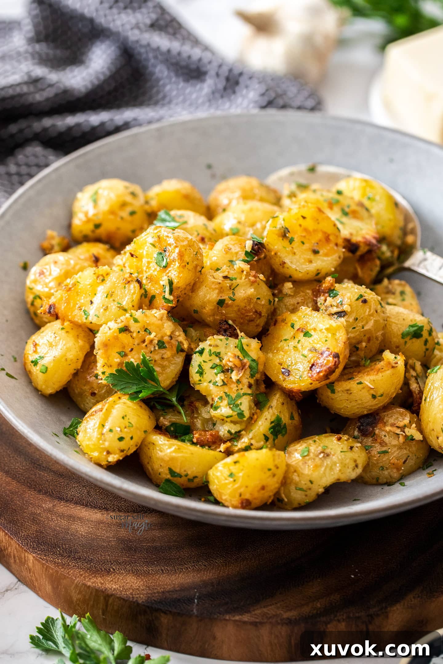 A grey bowl filled with raoasted potatoes on a wooden platter, garnished with parsley.