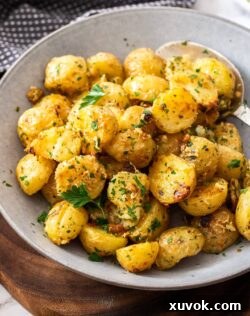 A grey bowl filled with raoasted potatoes. Golden brown and crispy, sprinkled with fresh herbs.