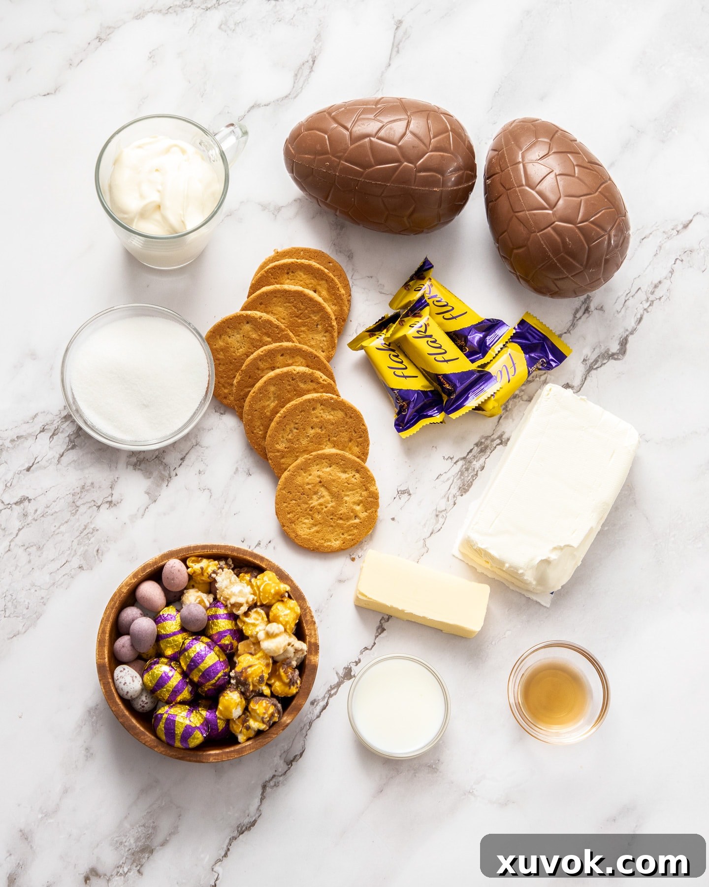 A flat lay photograph displaying all the ingredients required for making Easter egg cheesecakes on a light marble countertop.