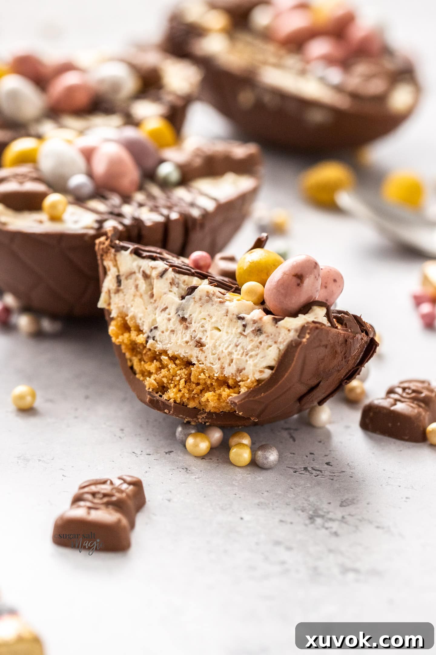 A close-up view of an Easter egg cheesecake cut in half, revealing the distinct layers of cookie crust, creamy cheesecake filling, and festive toppings.