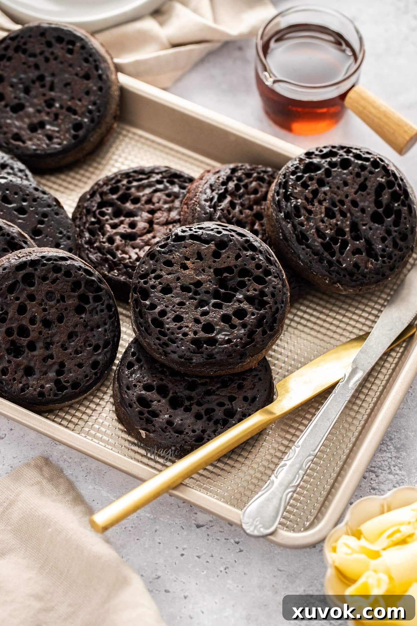 A batch of chocolate crumpets neatly arranged on a baking tray, ready to be stored or served. Their rich chocolate color and inviting holes are prominent.