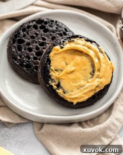 Two crumpets on a small plate, smothered in peanut butter.
