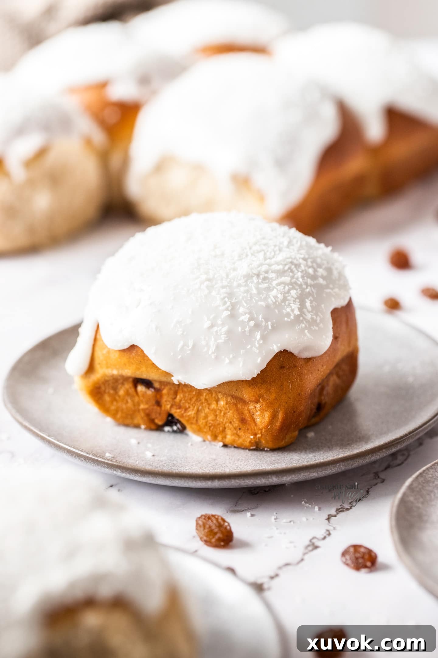 A sweet bun topped with white icing on a small dessert plate.