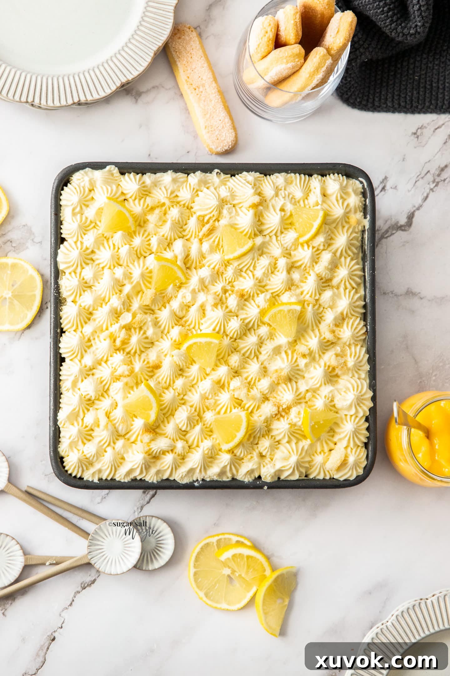 Top down view of lemon tiramisu in a pan surrounded by lemon slices and plates.