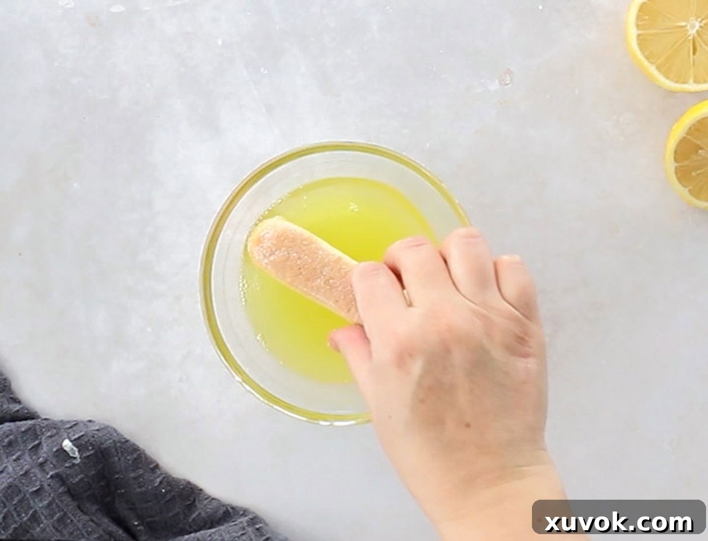 A hand dunking a savoiardi biscuit into limoncello.