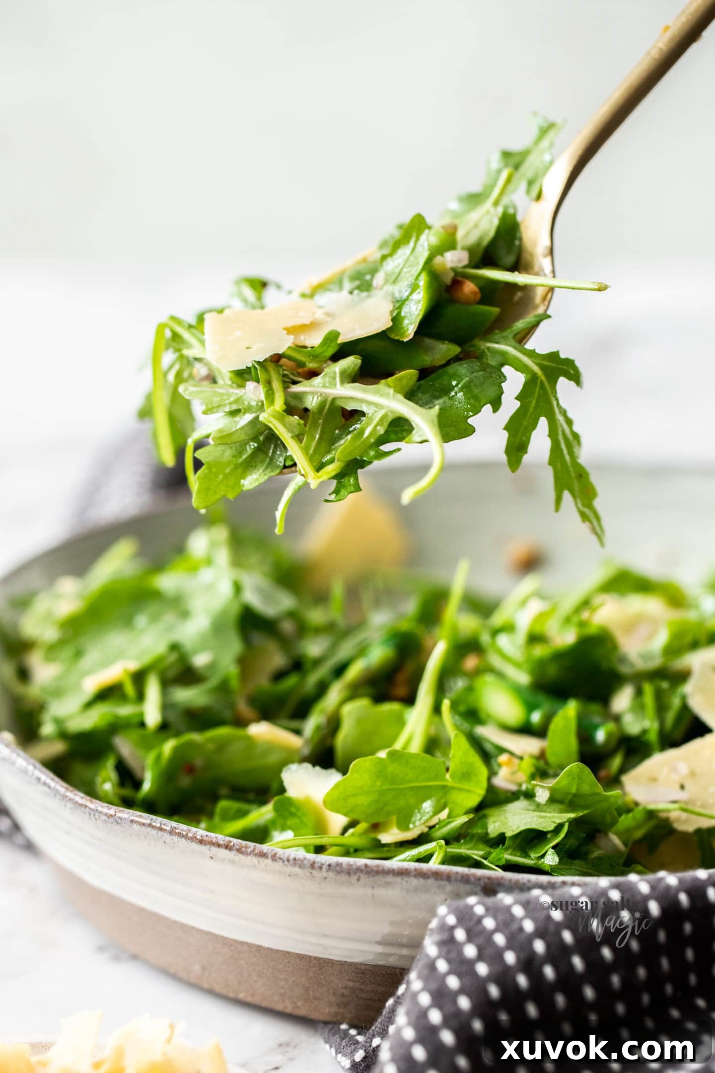 A single gold spoon holding a portion of vibrant rocket and parmesan salad.