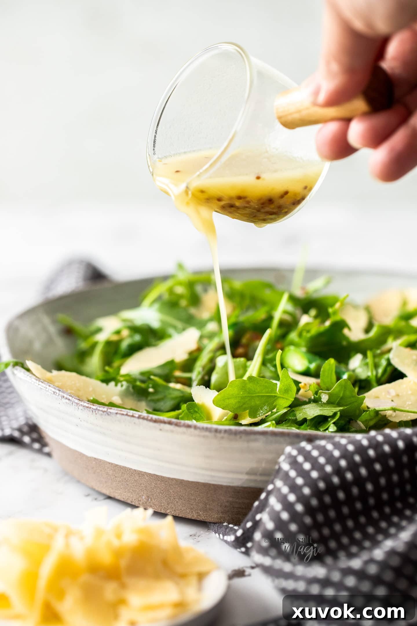 Lemon Mustard dressing being poured over a bowl of rocket and parmesan salad, highlighting the vibrant colors and fresh ingredients.