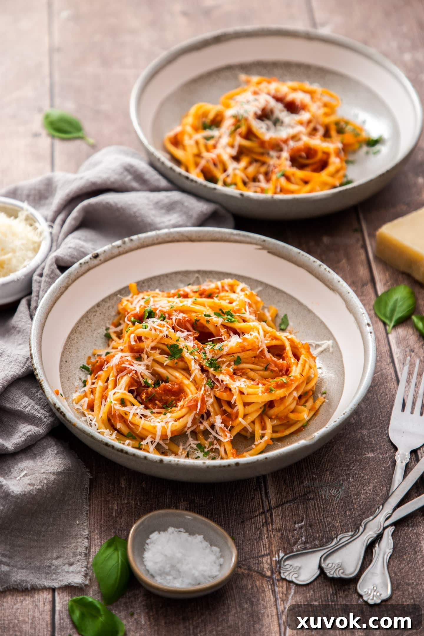 Two bowls filled with vibrant red pasta Napoletana, generously garnished with fresh basil leaves, arranged artfully on a rustic wooden table. The steam gently rises from the hot pasta, highlighting its inviting and homemade appeal, promising a comforting Italian meal.