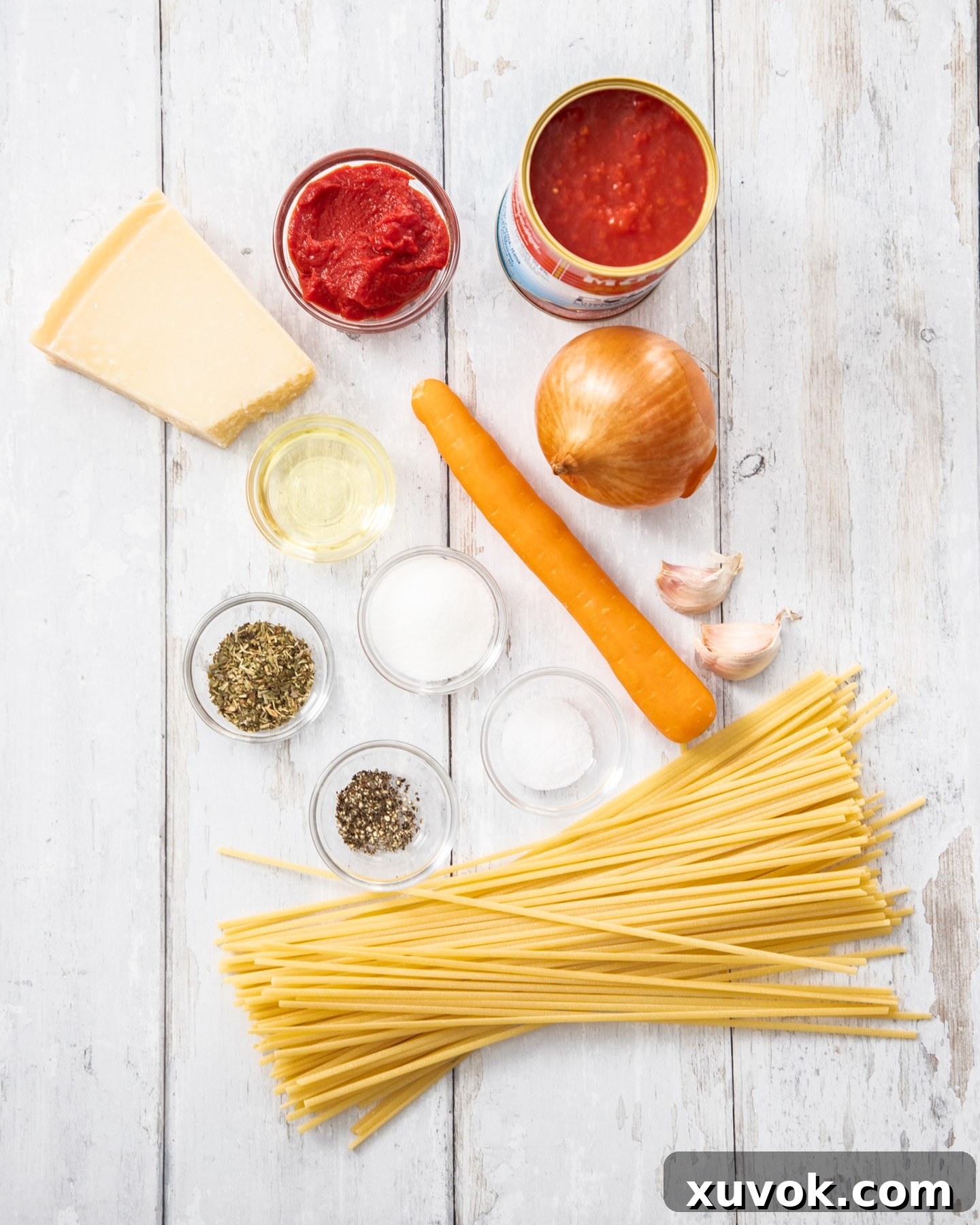 A collection of fresh ingredients for Pasta Napoletana neatly arranged on a rustic wooden countertop. The layout includes canned tomatoes, fragrant fresh basil, bulbs of garlic, a brown onion, and various pasta shapes like spaghetti and linguine, all signaling a vibrant cooking preparation.